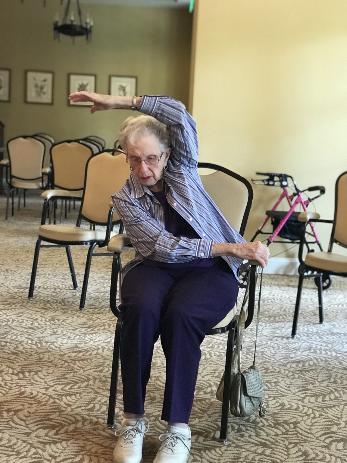 An older adult practicing a seated side stretch in chair yoga