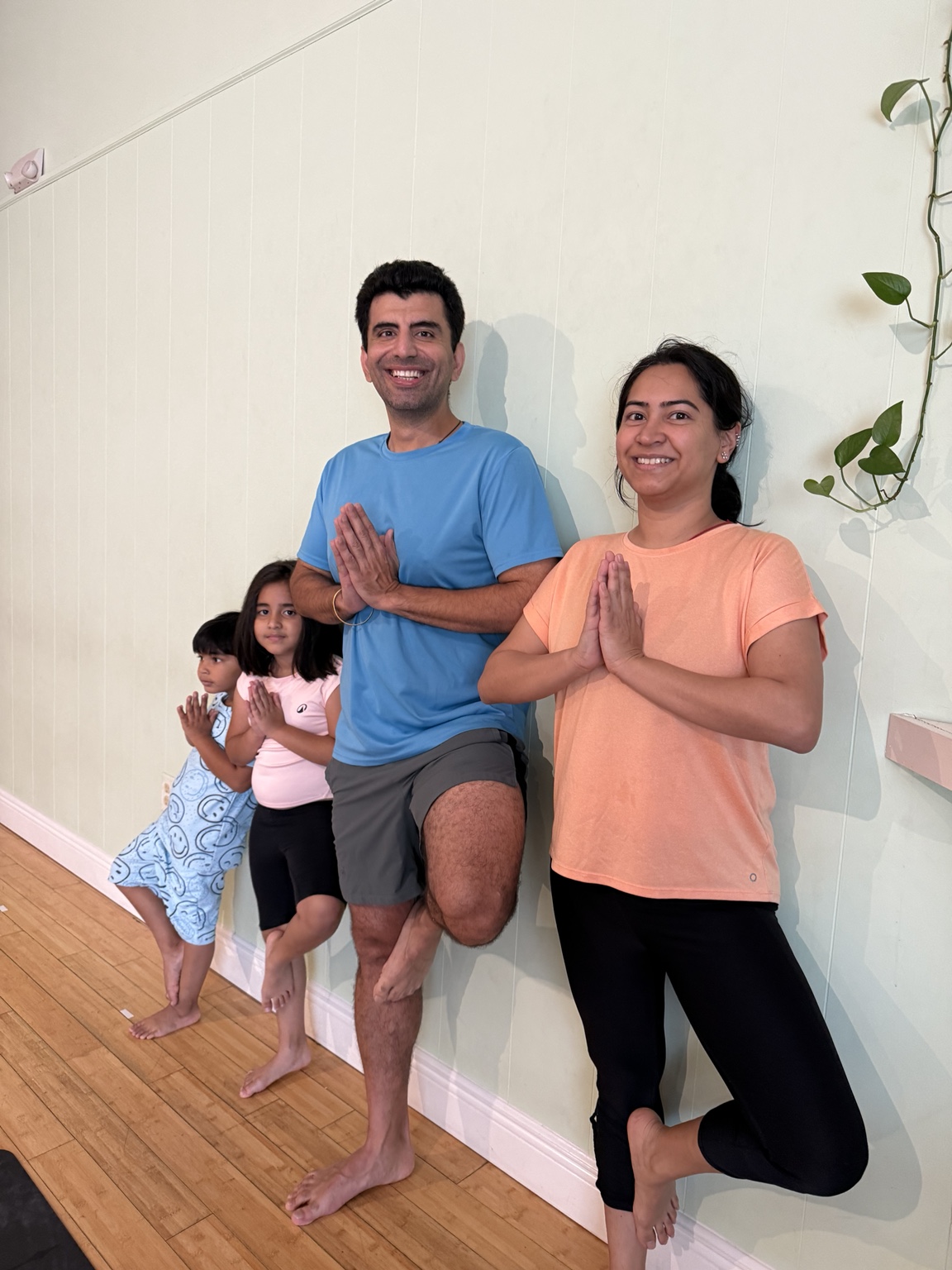 Two parents and two children smiling while practicing supported tree pose together