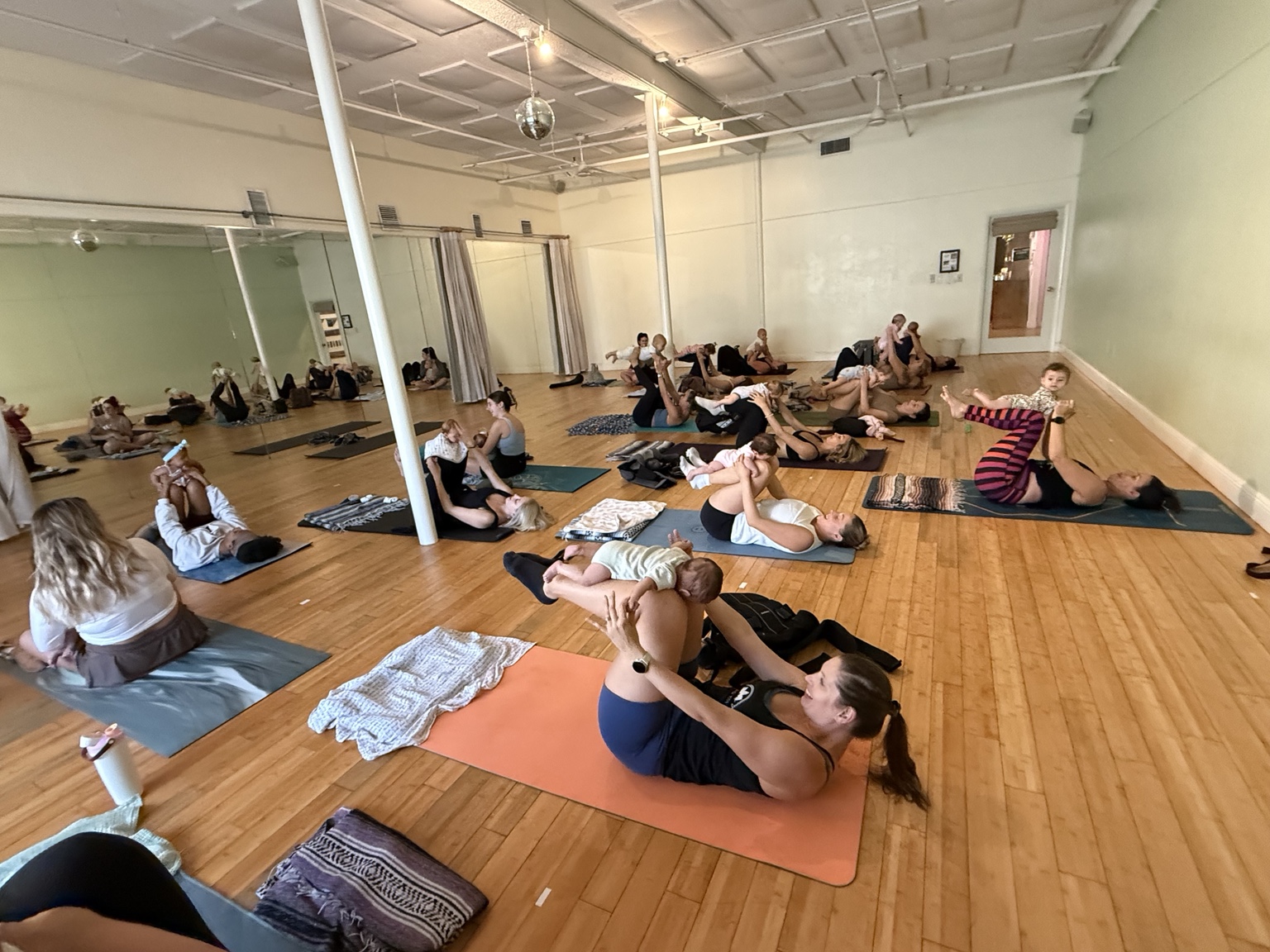 A large community class of parents practicing yoga while holding their babies