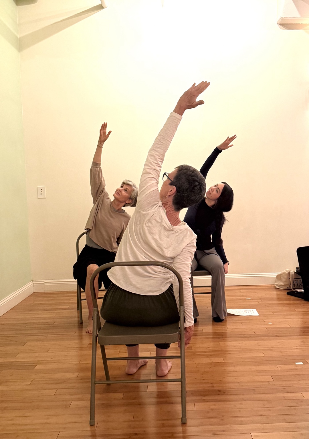 Three older adults practicing a seated side stretch together in chair yoga